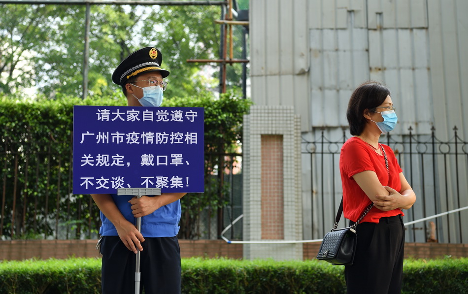2021年6月7日，广州，华师附中考点，一位手持安全提示牌的城管人员和一位考生家长。疫情影响下，考点外不再有大规模家长聚集送考的场景。